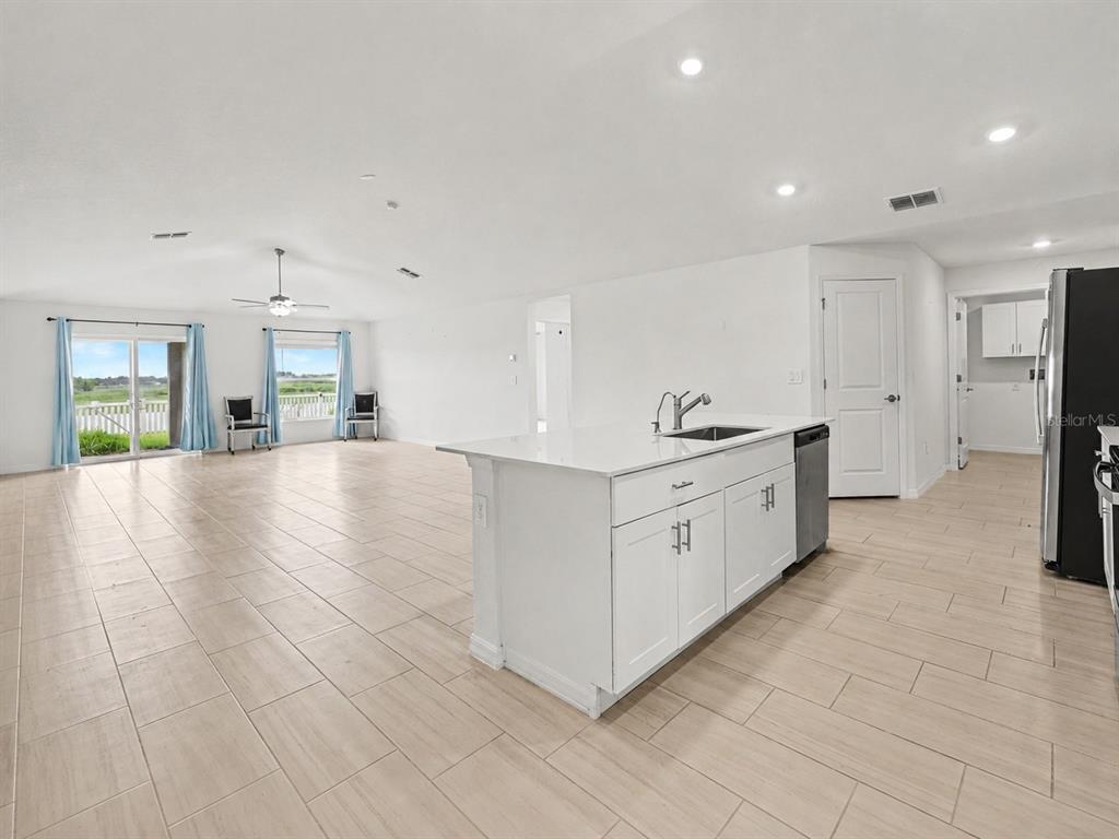 A bright open-concept kitchen and living area features white cabinetry, an island, and tile flooring — 15281 ZIRCON RED DRIVE, WIMAUMA, FL