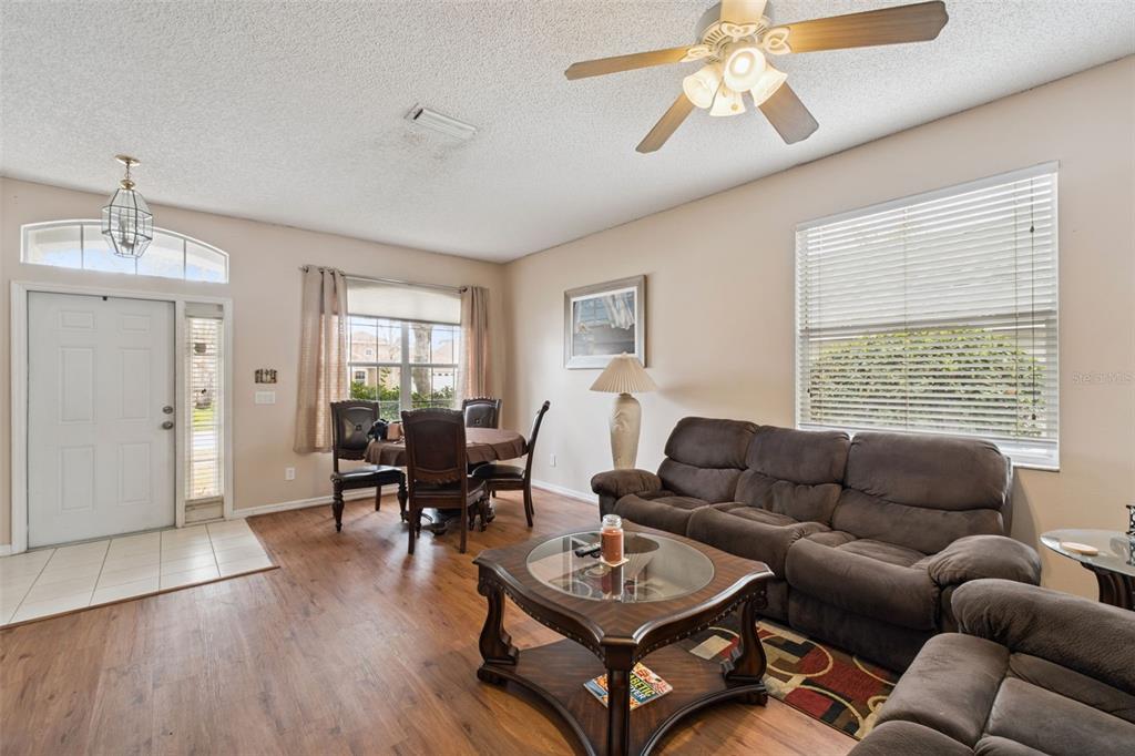 A living room with wood-look flooring, a brown sofa, a coffee table, and a dining area — 367 HICKORY SPRINGS PLACE, DEBARY, FL