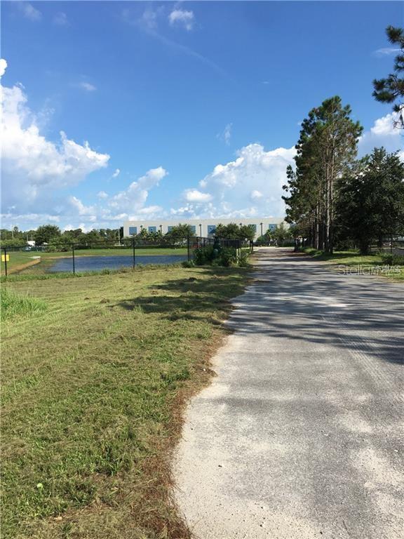 A gravel road leads past a grassy field and a pond toward a large industrial building — 857 JETSTREAM DRIVE LOT B, ORLANDO, FL
