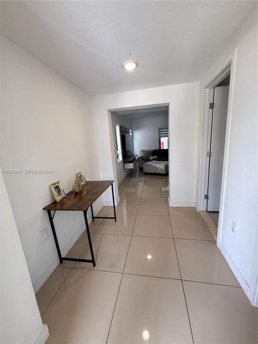 A hallway with large beige floor tiles leads into a living room with a sofa — 102 NW 10th Pl, Florida City FL 33034, FLORIDA CITY, FL