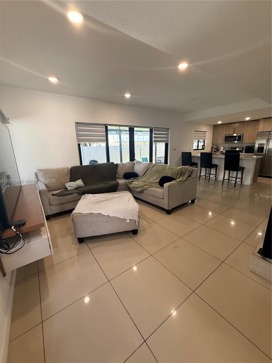 This open-concept living room features light-colored tile flooring, a sectional sofa, and a kitchen island — 102 NW 10th Pl, Florida City FL 33034, FLORIDA CITY, FL
