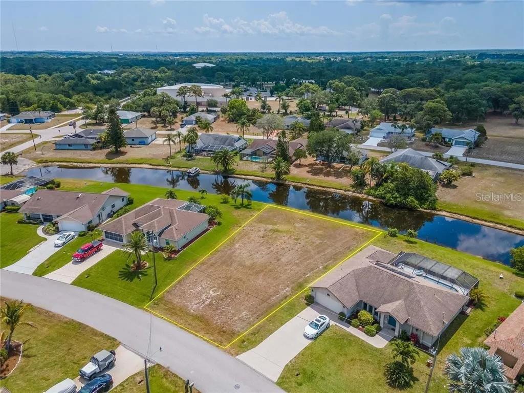An aerial view shows a vacant residential lot situated between two houses along a canal — 129 BUNKER ROAD, ROTONDA WEST, FL