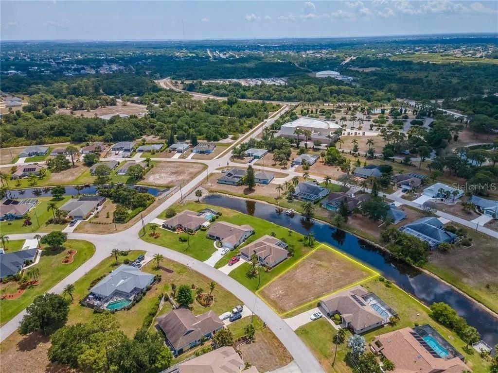 An aerial view shows a vacant residential lot bordered by a canal and suburban houses — 129 BUNKER ROAD, ROTONDA WEST, FL