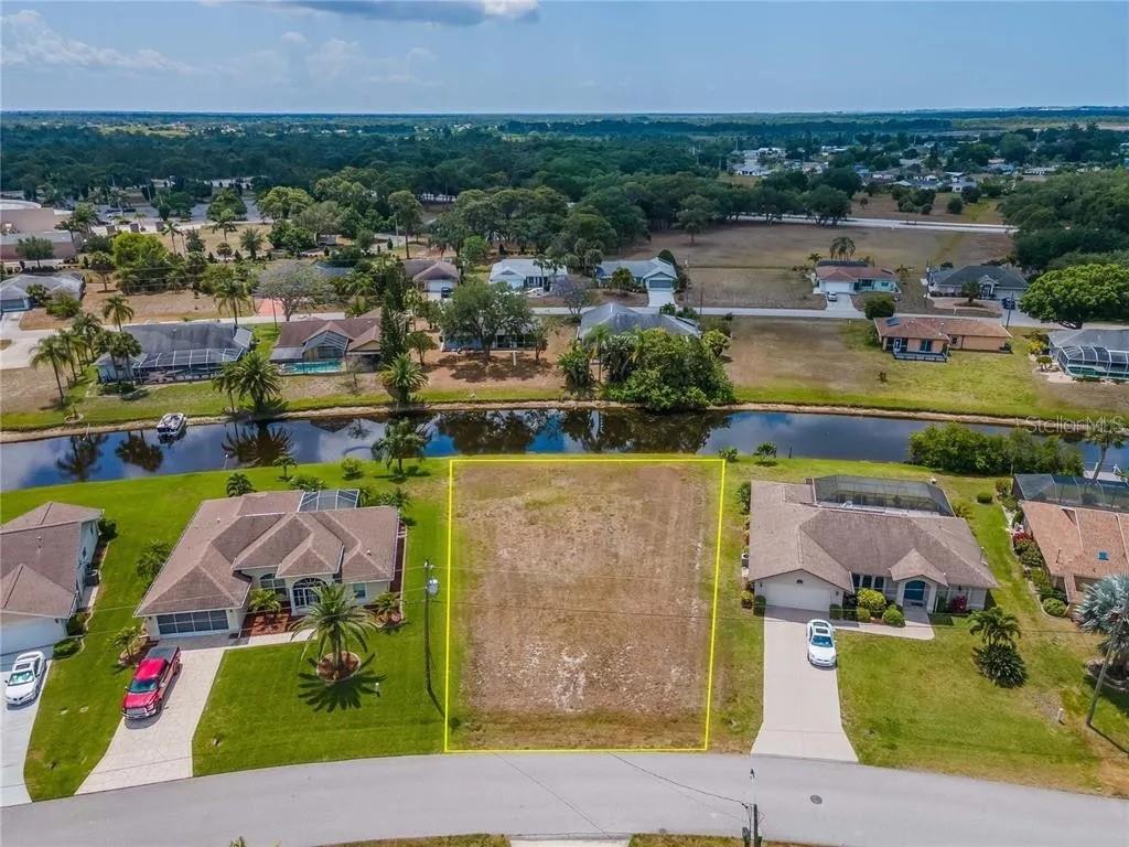 An aerial view shows a vacant residential lot situated between two houses along a canal — 129 BUNKER ROAD, ROTONDA WEST, FL
