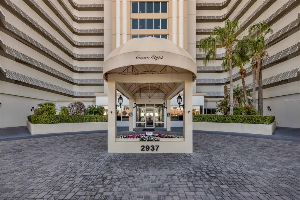 The exterior entrance of a multi-story condominium building features a covered porte-cochère and landscaping — 2937 S ATLANTIC AVENUE UNIT 206, DAYTONA BEACH SHORES, FL