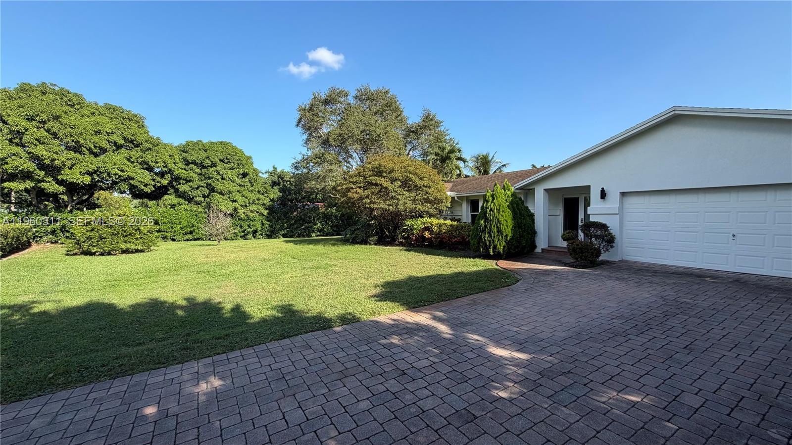 A white house with a paved driveway and a large green lawn under blue skies — 11030 SW 42nd Ct, Davie FL 33328, DAVIE, FL