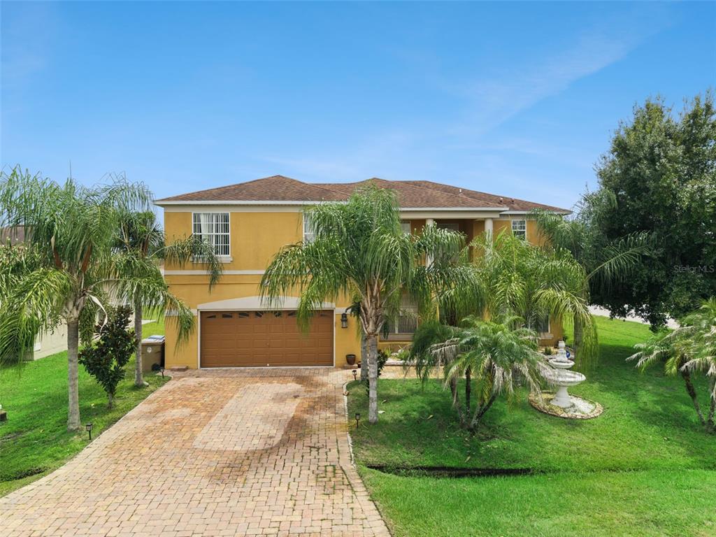 A two-story yellow house with a paved driveway, palm trees, and a front yard fountain — 331 ASHBURTON WAY, KISSIMMEE, FL