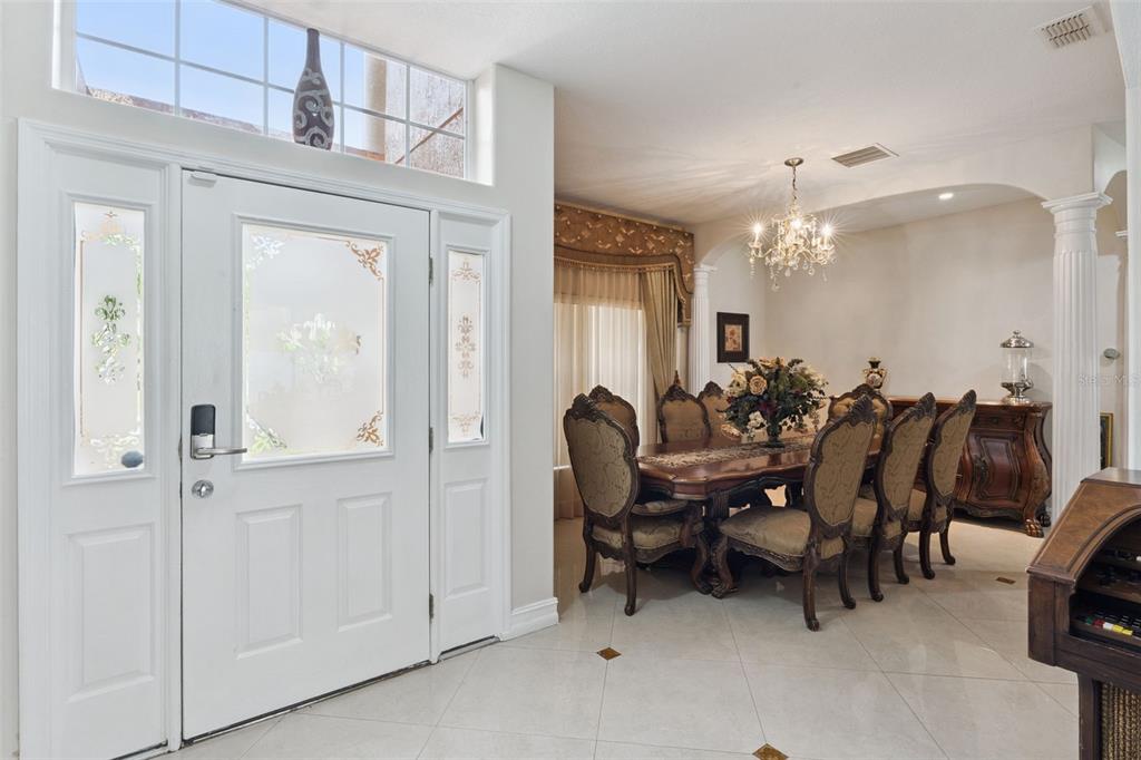 A white front door with glass panels opens into a dining room with a chandelier — 331 ASHBURTON WAY, KISSIMMEE, FL