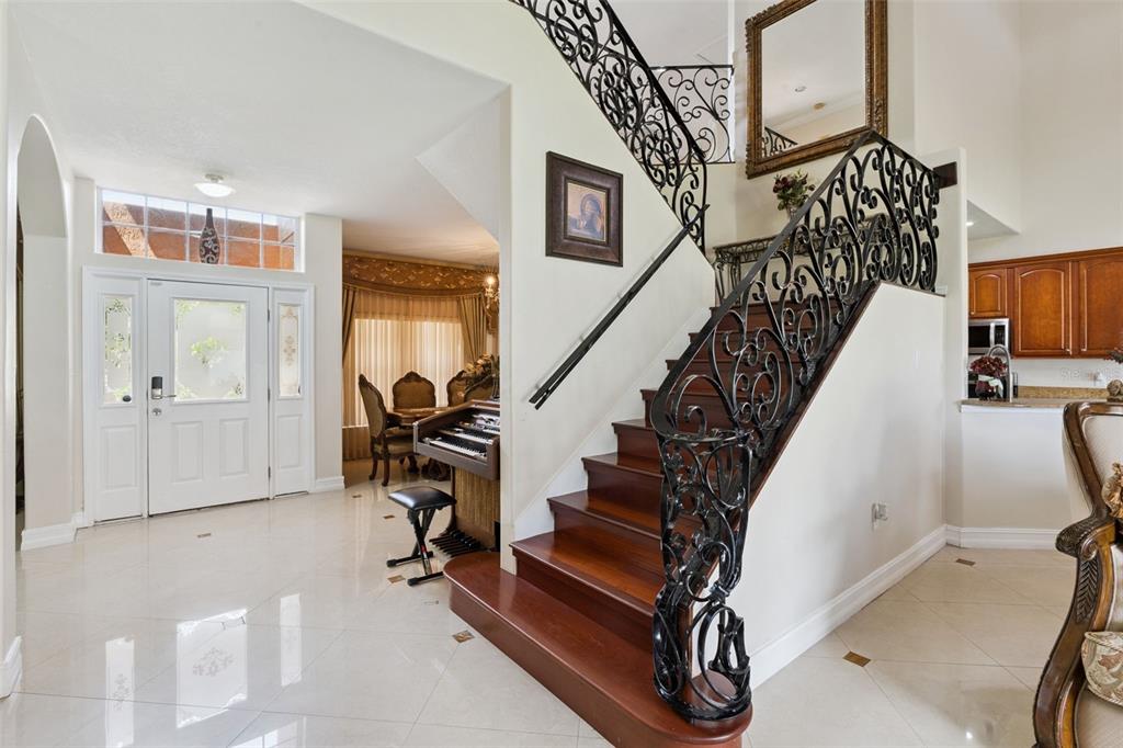 An entryway features a wooden staircase with ornate iron railings, tile flooring, and a piano — 331 ASHBURTON WAY, KISSIMMEE, FL