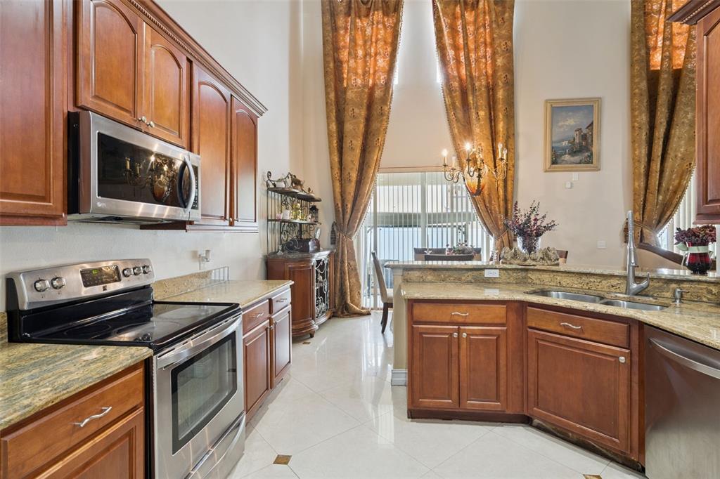 A kitchen with wood cabinets, granite countertops, stainless steel appliances, and tall gold curtains — 331 ASHBURTON WAY, KISSIMMEE, FL