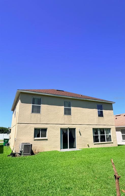 The rear exterior of a two-story beige house features a sliding glass door and lawn — 32111 BROOKSTONE DRIVE, WESLEY CHAPEL, FL