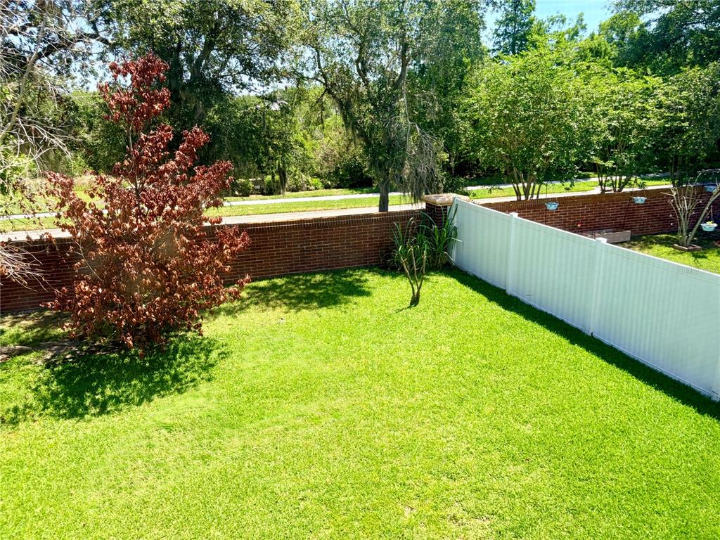 A backyard features a green lawn, a brick wall, and a white vinyl privacy fence — 32111 BROOKSTONE DRIVE, WESLEY CHAPEL, FL