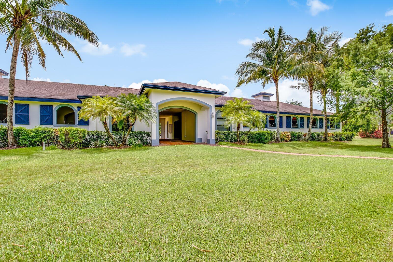 A single-story building with a central arched entryway, blue trim, and surrounding palm trees — 5656 South Shore Boulevard, Wellington FL 33449, WELLINGTON, FL