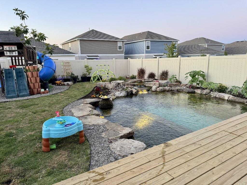 A backyard features a natural stone pond with a waterfall, a wooden deck, and playground equipment — 5511 BRAKEN FERN WAY, LEESBURG, FL