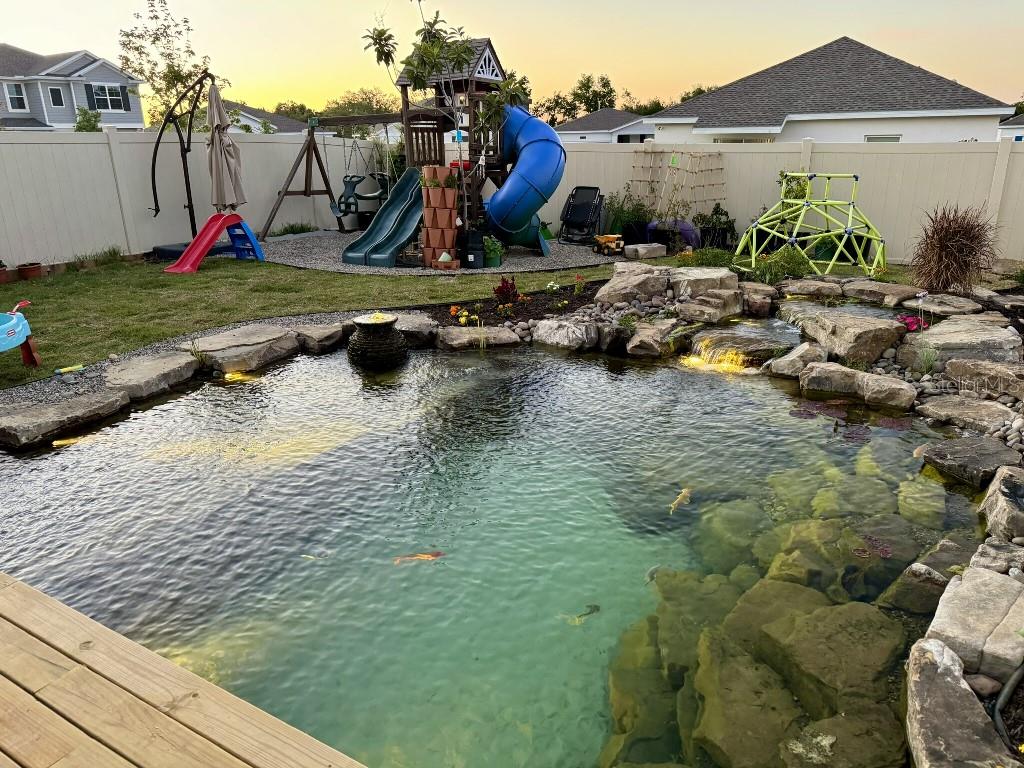 A backyard features a large koi pond with a waterfall and a nearby playground set — 5511 BRAKEN FERN WAY, LEESBURG, FL