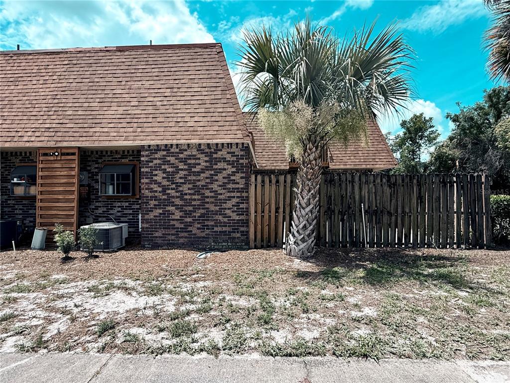 A brick exterior wall with a wooden fence and a palm tree in the yard — 202 TERRACE COURT, SANFORD, FL