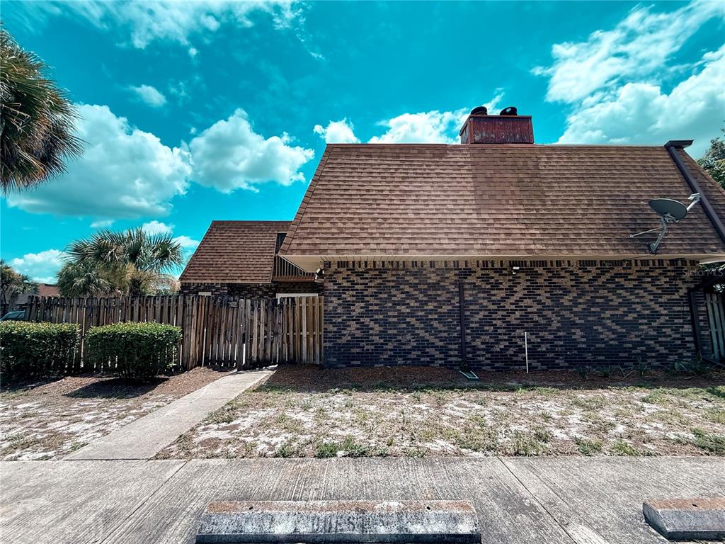 A brick building with a brown shingled roof stands behind a wooden fence and sidewalk — 202 TERRACE COURT, SANFORD, FL