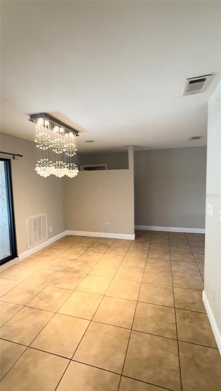 An empty room features tan tile flooring, light gray walls, and a modern crystal chandelier — 3109 RESEDA COURT, TAMPA, FL