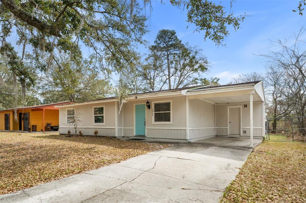 A single-story house with light-colored siding, a turquoise front door, and an attached carport — 1911 SE 14TH AVENUE, GAINESVILLE, FL