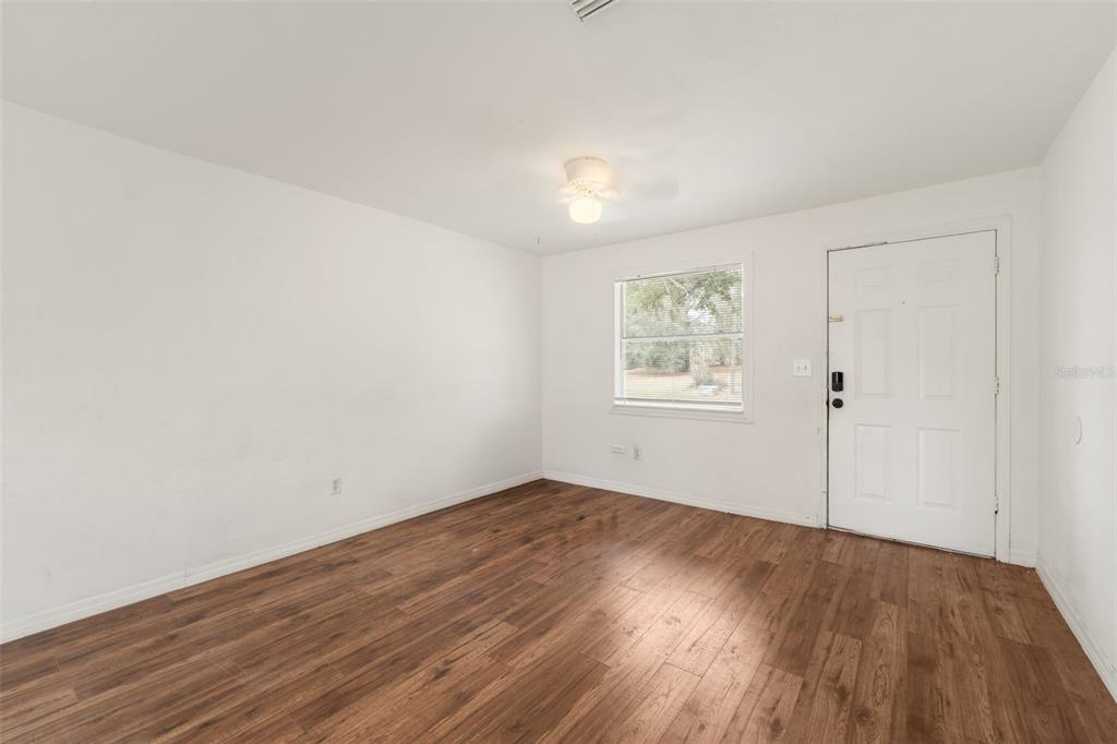 An empty room features white walls, wood-look flooring, a ceiling fan, and an exterior door — 1911 SE 14TH AVENUE, GAINESVILLE, FL