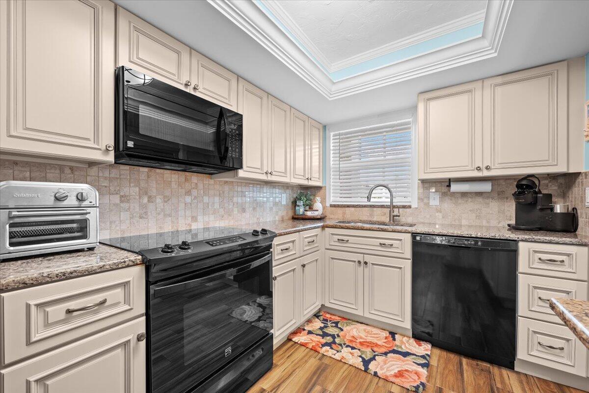 A kitchen features cream cabinets, granite countertops, a tiled backsplash, and black appliances — 1205 Sandy Lane # 145, Singer Island FL 33404, SINGER ISLAND, FL