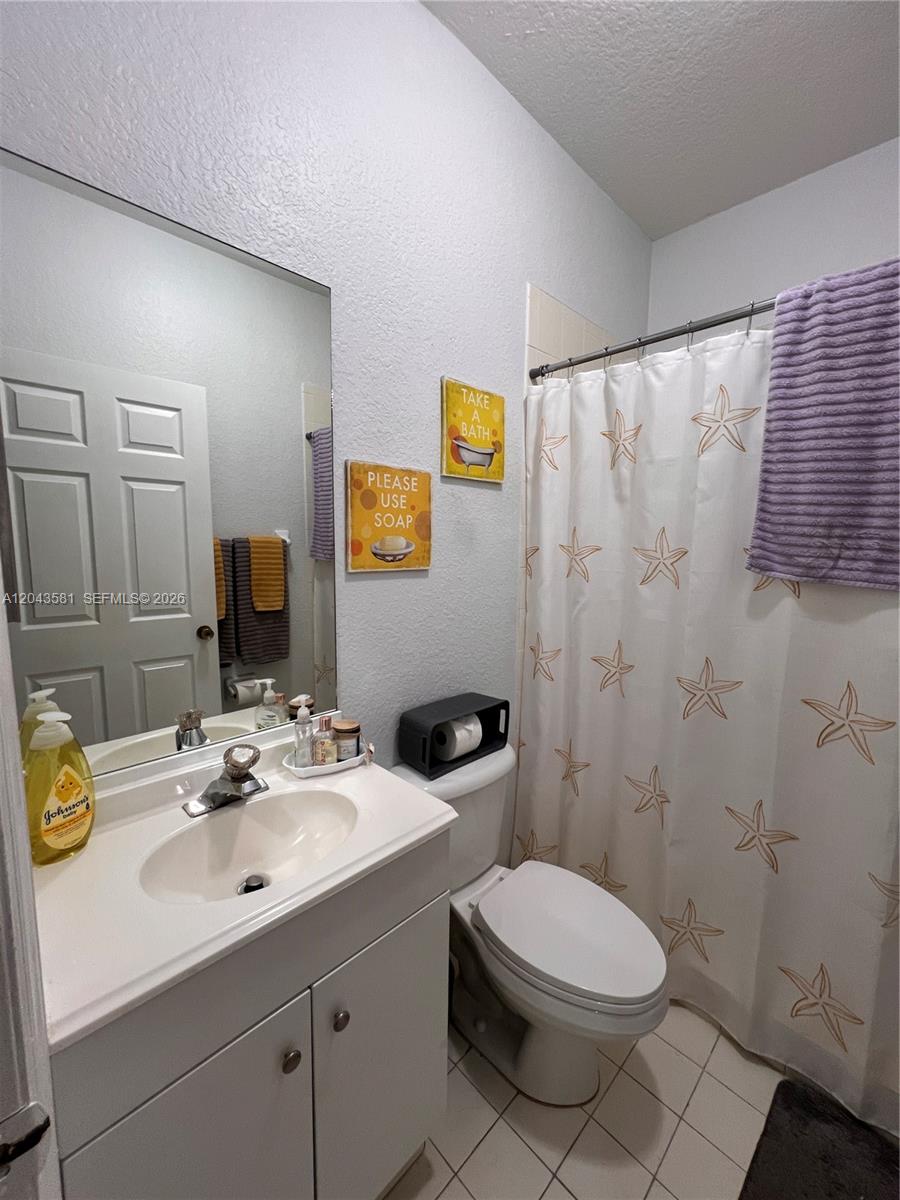 A bathroom features a white vanity, a toilet with a black holder, and a starfish-patterned curtain — TAMARAC, FL