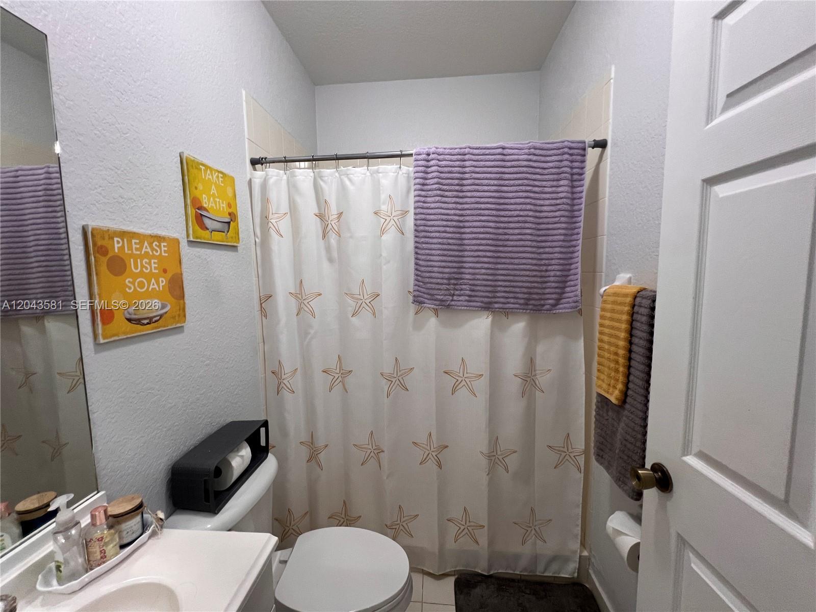 A bathroom features a starfish-patterned shower curtain, a toilet, and wall-mounted decorative signs — TAMARAC, FL