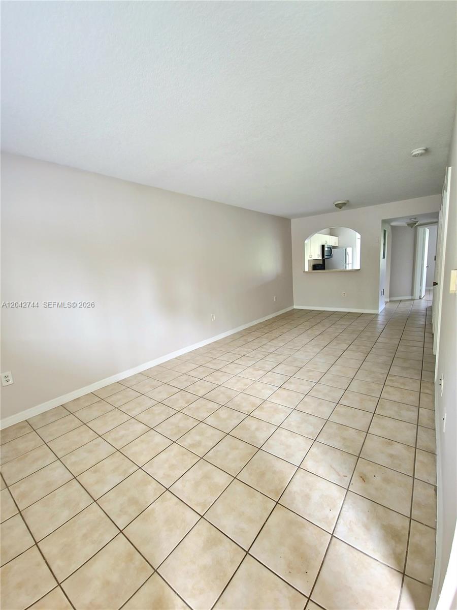 An empty room features beige tile flooring, light-colored walls, and a pass-through to the kitchen — 3398 NE 9th Dr # 102, Homestead FL 33033, HOMESTEAD, FL