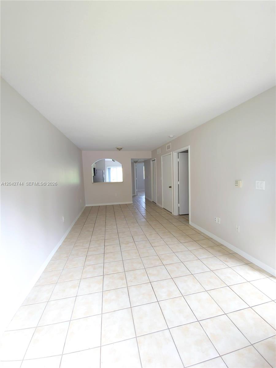An empty room features light-colored tile flooring, plain walls, and an arched pass-through window — 3398 NE 9th Dr # 102, Homestead FL 33033, HOMESTEAD, FL