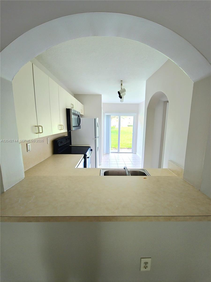 A kitchen with light-colored cabinets and a pass-through window overlooks a bright dining area — 3398 NE 9th Dr # 102, Homestead FL 33033, HOMESTEAD, FL