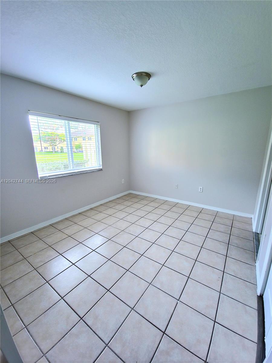 An empty room features light-colored walls, a window, and beige square floor tiles — 3398 NE 9th Dr # 102, Homestead FL 33033, HOMESTEAD, FL