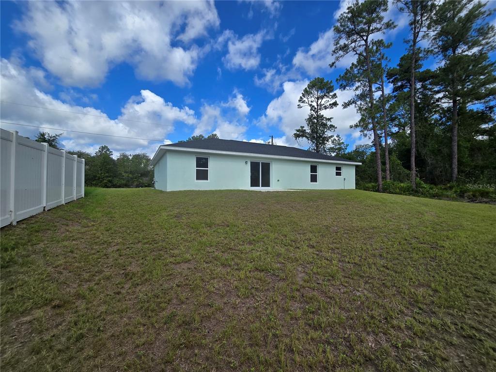 The exterior rear view of a light-colored house features a sliding glass door and windows — 35 SEQUOIA TRAIL, OCKLAWAHA, FL