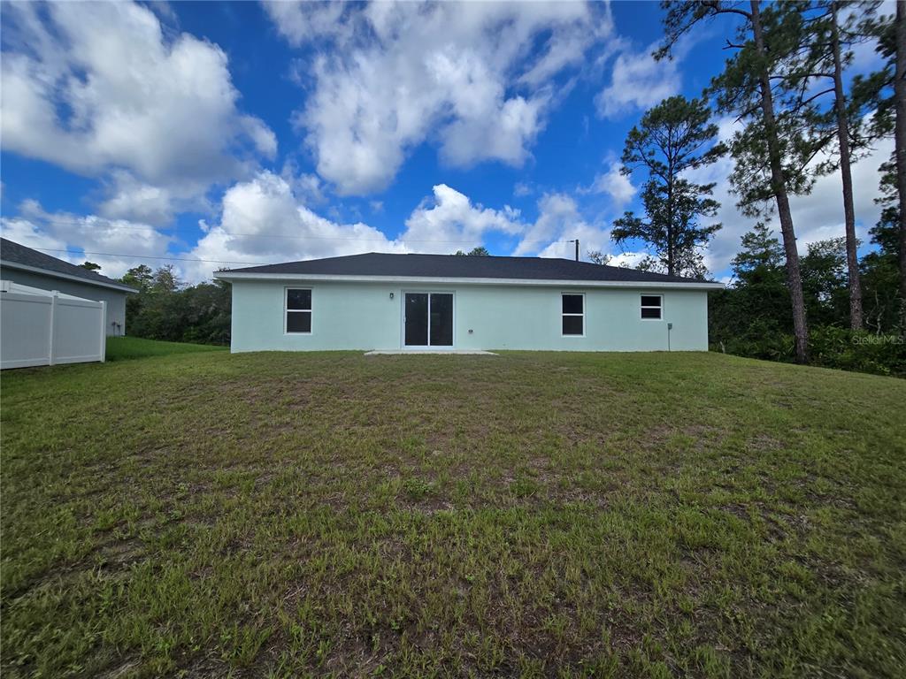 The rear exterior of a single-story house features a light-colored facade, sliding doors, and windows — 35 SEQUOIA TRAIL, OCKLAWAHA, FL