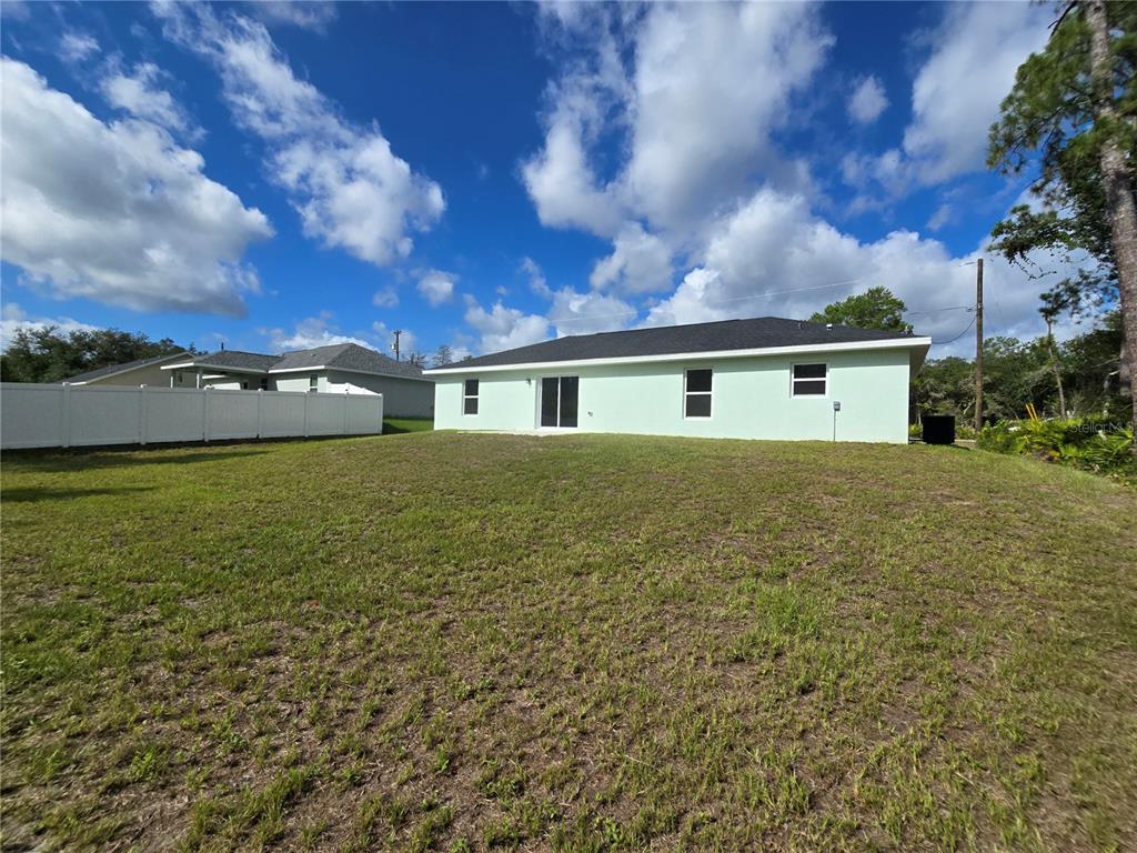 The back exterior of a light green house features a sliding glass door and windows — 35 SEQUOIA TRAIL, OCKLAWAHA, FL