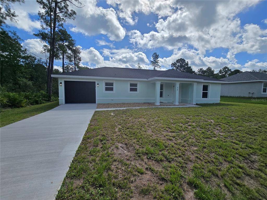 A light green single-story house with a dark garage door and a concrete driveway — 35 SEQUOIA TRAIL, OCKLAWAHA, FL