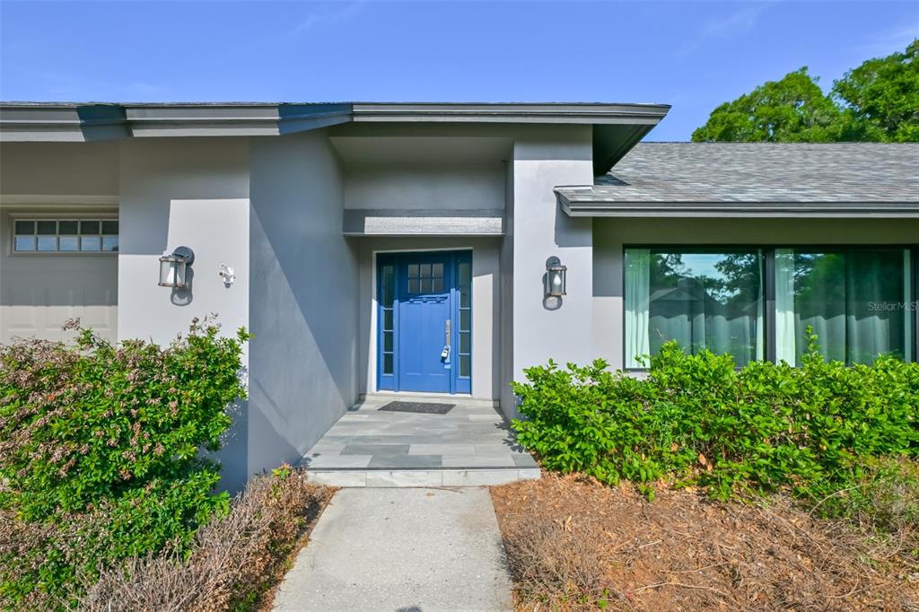 The exterior of a house features a blue front door, gray siding, and green bushes — 2701 HERNDON STREET, VALRICO, FL