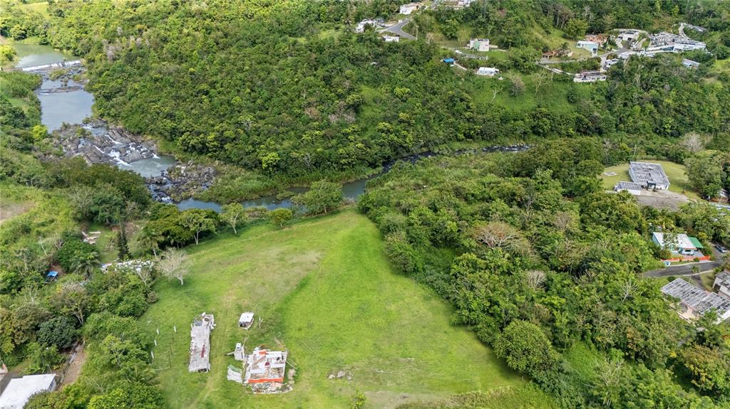An aerial view shows a grassy lot with a small structure near a winding river — TRAZO BARRIO RINCON, CIDRA, PR