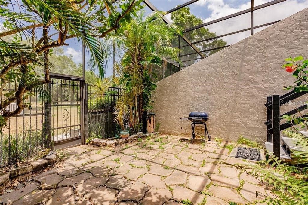 A screened-in stone patio features a small charcoal grill, lush greenery, and a metal gate — 323 BOBBY JONES ROAD UNIT 323, SARASOTA, FL