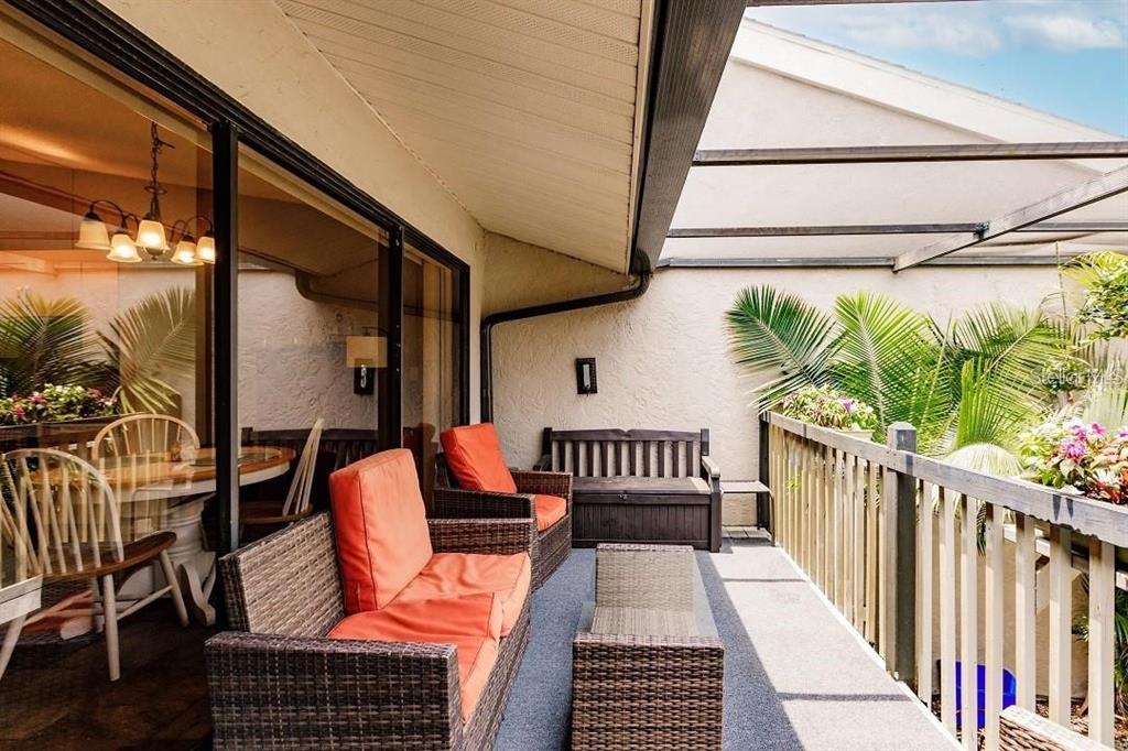 A covered balcony features wicker furniture with orange cushions and a wooden bench — 323 BOBBY JONES ROAD UNIT 323, SARASOTA, FL