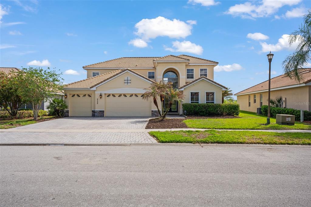 A two-story suburban house with a tan stucco exterior, tile roof, and three-car garage — 3790 EAGLE ISLE CIRCLE, KISSIMMEE, FL