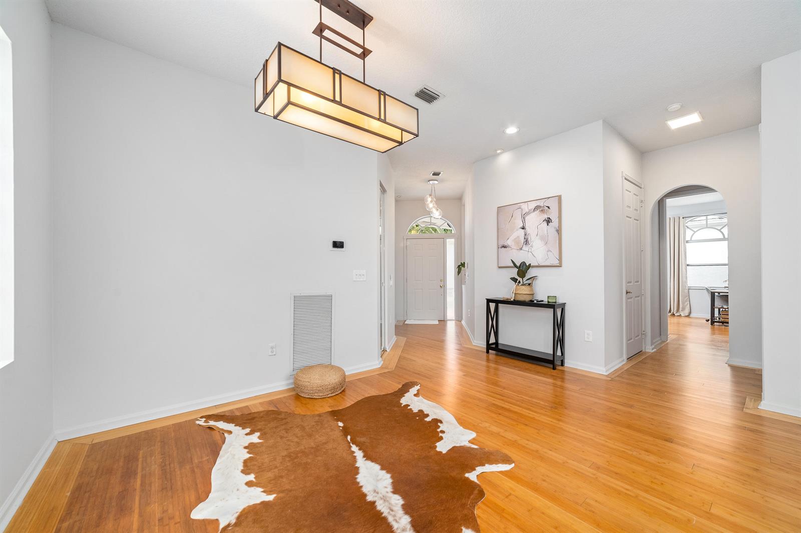 A bright entryway features hardwood floors, a cowhide rug, and a modern rectangular pendant light — 2072 Chagall Circle, West Palm Beach FL 33409, WEST PALM BEACH, FL
