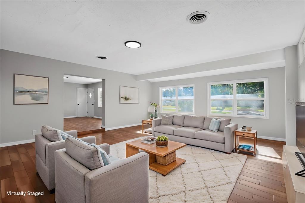 A living room with light gray walls, wood flooring, a beige sofa, and two armchairs — 4600 NE 22ND AVENUE, OCALA, FL