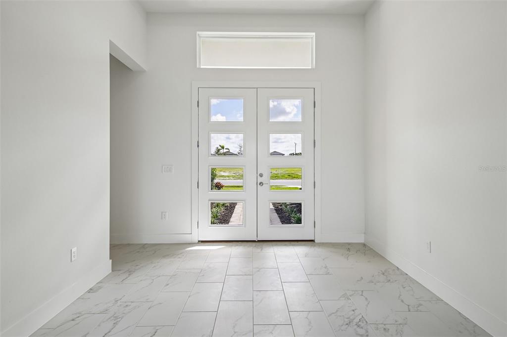 A bright entryway features white walls, marble-look tile flooring, and double glass-paneled front doors — 8255 GOLDEN BEACH COURT, PARRISH, FL