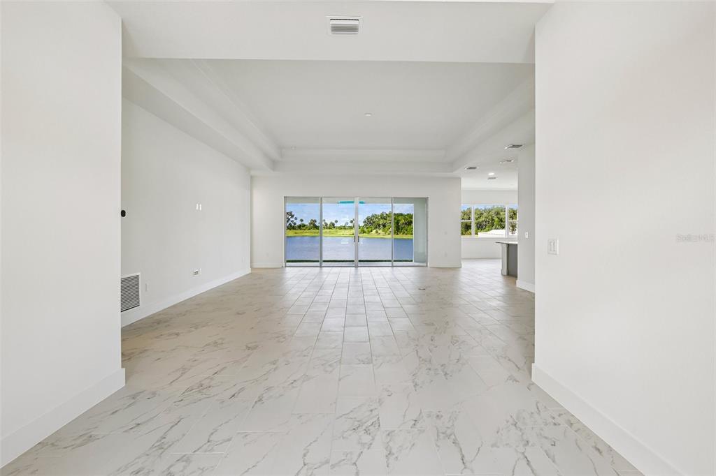 An open-concept living area features white marble-look tile flooring and sliding glass doors overlooking water — 8255 GOLDEN BEACH COURT, PARRISH, FL