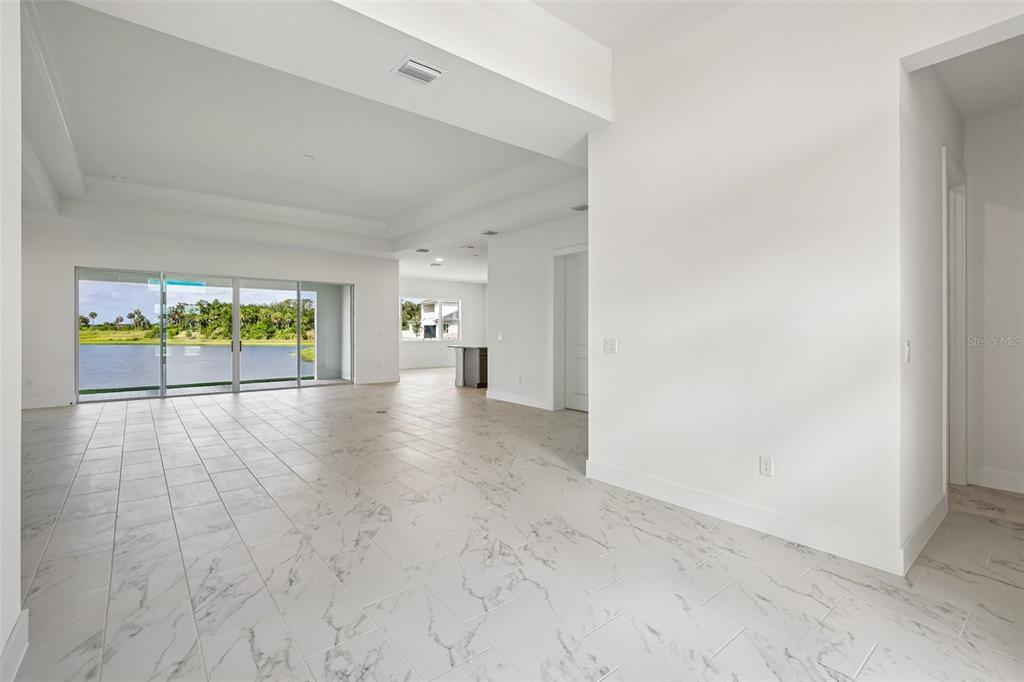 An open-concept living area features white marble-look tile flooring and sliding glass doors overlooking water — 8255 GOLDEN BEACH COURT, PARRISH, FL