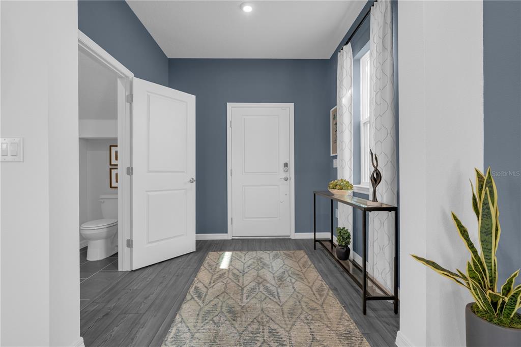 An entryway features blue walls, gray wood-look flooring, a white front door, and a console table — 4442 RIVER BEACON BOULEVARD, DAVENPORT, FL