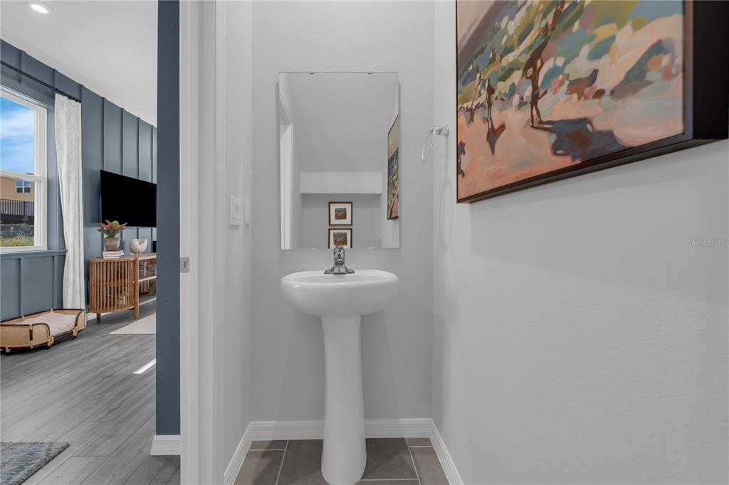 A small powder room features a white pedestal sink, a wall mirror, and gray tile flooring — 4442 RIVER BEACON BOULEVARD, DAVENPORT, FL