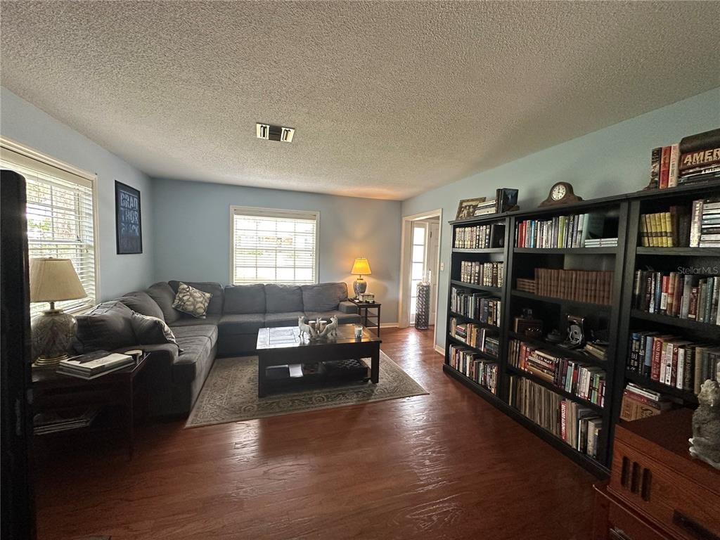 A living room features a grey sectional sofa, a coffee table, and large black bookshelves — 1105 S 9TH STREET, LEESBURG, FL