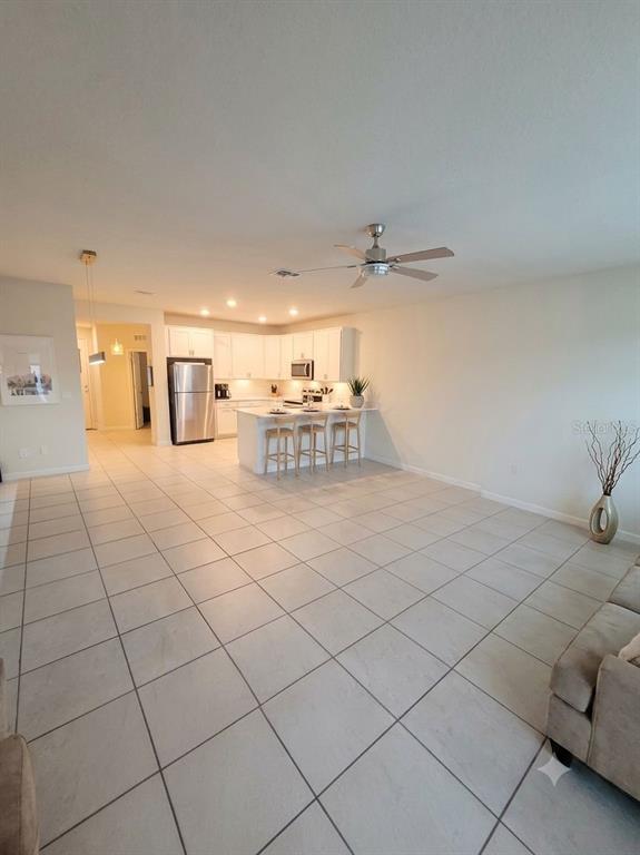 An open-concept kitchen with white cabinetry and a breakfast bar overlooks a tiled living area — 9740 BROWN BURROW STREET, ORLANDO, FL