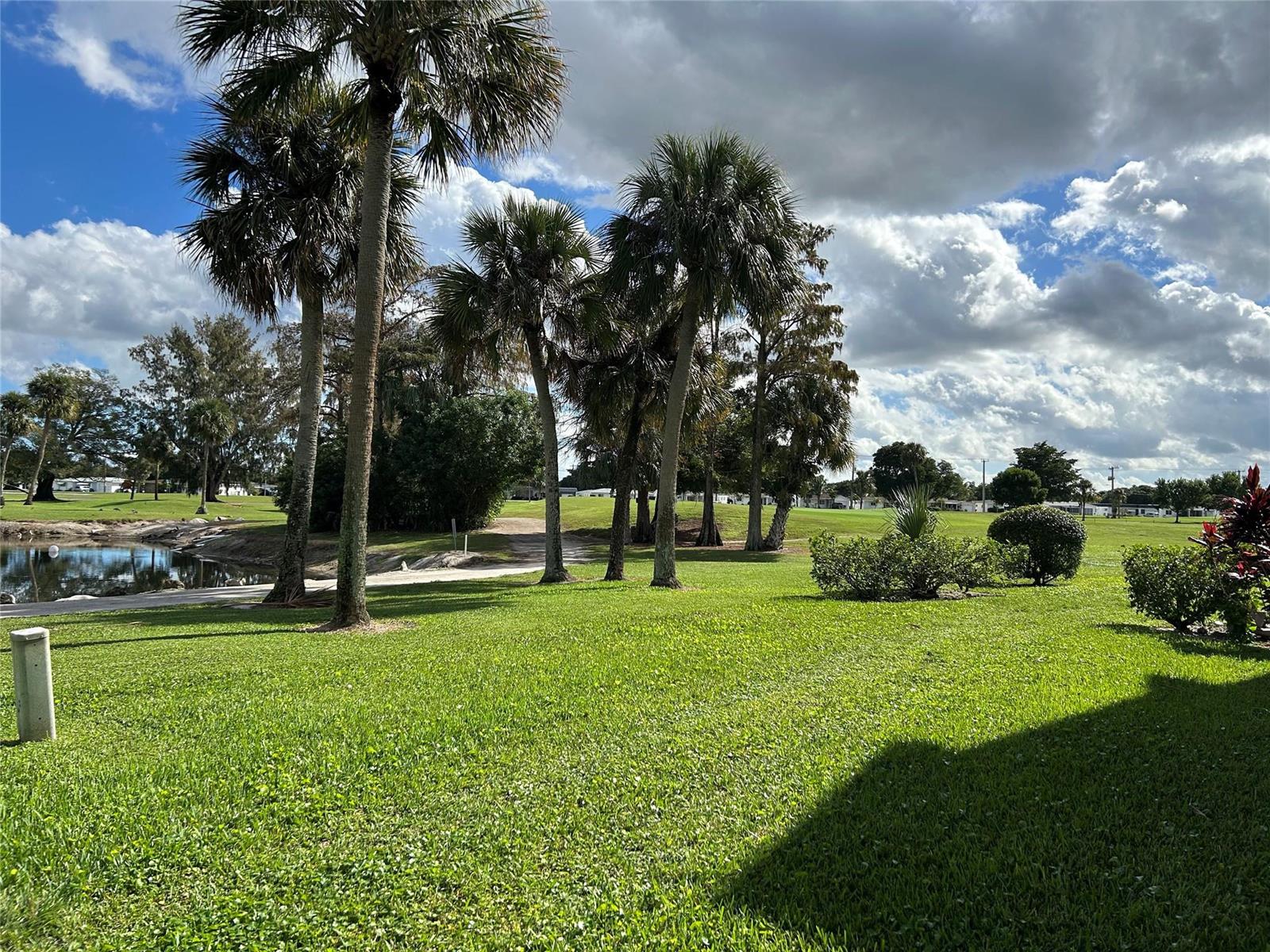 A grassy lawn features several palm trees and a small pond under a cloudy sky — 7807 Golf Circle Drive # 205, Margate FL 33063, MARGATE, FL